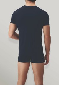 T-shirt blu navy a maniche corte, tessuto morbido, vestibilità comoda, abbinato a pantaloni corti attillati in tinta, visto da dietro su uno sfondo chiaro.