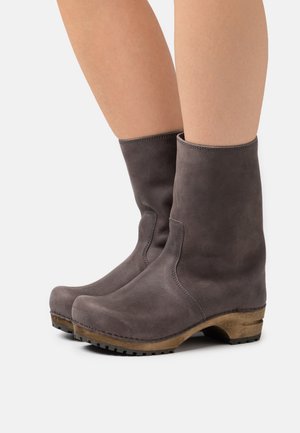 Botas de cuero gris hasta el tobillo con una textura suave, punta redondeada y un tacón apilado de estilo madera. Detalle de costura a lo largo de las costuras.