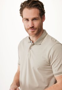 Beige polo t-shirt med en blød tekstur, udstyret med en klassisk krave, to knapper og kontrasterende detaljer på manchetterne.