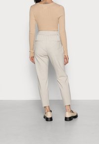 Béžový žebrovaný top s dlouhým rukávem a kulatým výstřihem, zkombinovaný se světle béžovými elegantními kalhotami s páskem v pase a hladkými kapsami.
