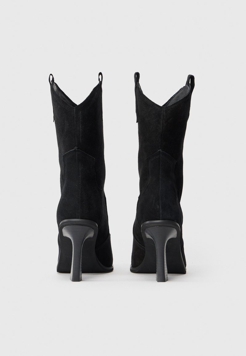 Stivaletti neri in suede con punta affilata, tacco a stiletto alto e risvolti a forma di V. Presentano delle linguette per facilitare l'indossamento.