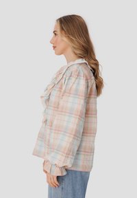 Blusa de cuadros colorida con cuello rizado y mangas abullonadas, en tonos pastel de rosa, azul y verde; tela ligera con una apariencia texturada.