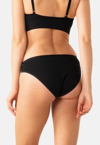 Ensemble de bralette en coton noir et de bikini. La bralette présente des bretelles fines. Le bikini possède une texture lisse et un design à jambe haute.