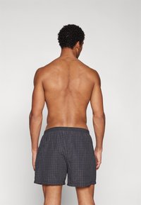 Men’s swim shorts in dark gray with a checkered pattern, elastic waistband, and a relaxed, loose fit. Suitable for water activities.