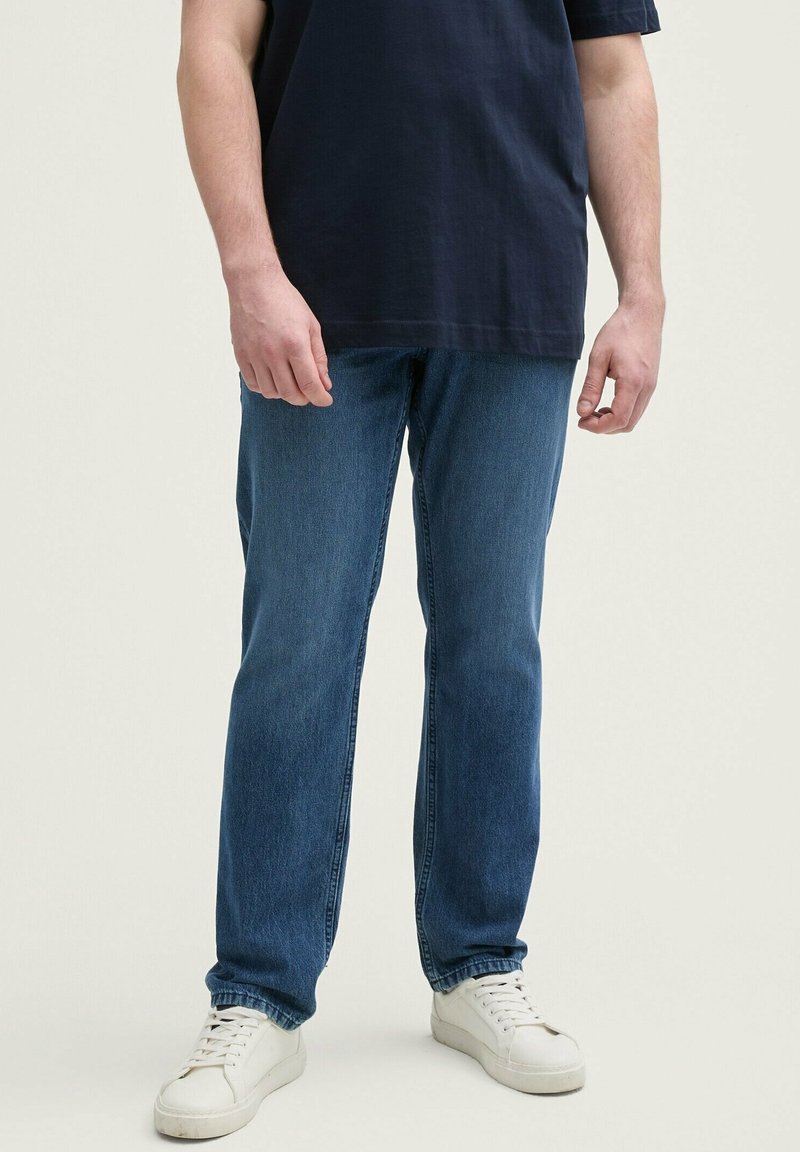 Jeans de mezclilla azul con un diseño de pierna recta, ligero desgaste y costuras de contraste. Combinados con zapatillas blancas.