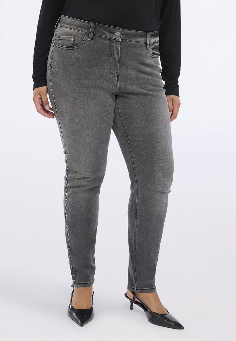 Jeans ajustados grises de cintura alta, con un ligero desgaste, detalles de botones en los laterales y una textura de denim elástico. Combinados con tacones negros puntiagudos.