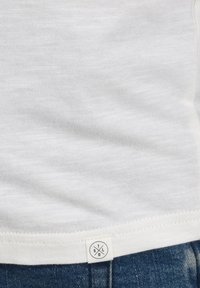Camisa blanca de manga corta hecha de tejido ligero y texturizado, que presenta una etiqueta de logo discreta en el dobladillo y un corte clásico.