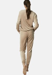 Beige velours loungewear set met een langemouwen top en broek met elastische tailleband en geribde boorden. Zachtere textuur, casual pasvorm.