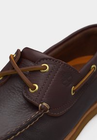 Κοντινή λήψη καφέ δερμάτινου παπουτσιού σκάφους με ταμπα κορδόνια περασμένα από χρυσά οπτικά και λεπτομερή ραφές κατά μήκος των ραφών.