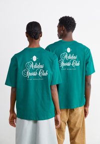 Grønne bomulds t-shirts med "Adidas Sports Club" i hvid skrift på ryggen, med korte ærmer og løs pasform.