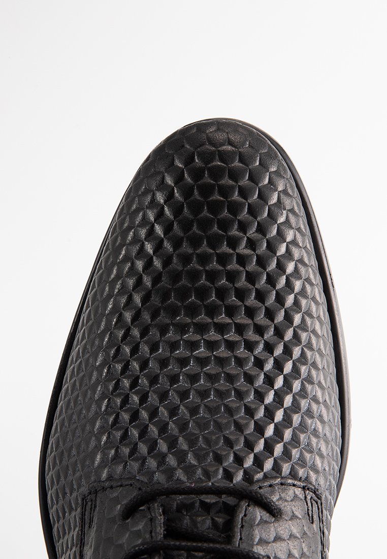 Zapato de cuero negro con un patrón texturizado en forma de panal en la parte superior, con punta redonda y diseño de cordones.