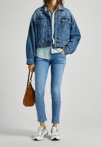 Kratší džísková bunda ve středně modré barvě, pod ní světle modrá košile na knoflíky, světle modré úzké džíny, hnědá semišová kabelka a šedé tenisky.