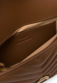 Intérieur d'un sac à main en cuir marron, présentant une texture lisse, un motif matelassé diagonal, des détails en matériel doré et une étiquette de marque emboutie à l'intérieur.