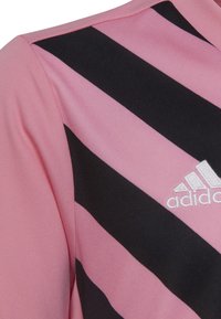 Camiseta deportiva rosa con franjas diagonales negras, hecha de tela texturizada, con un logo de Adidas bordado en blanco.