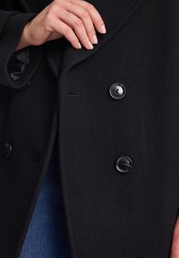 Czarny wełniany płaszcz z podwójnym zapięciem, gładką teksturą i dużymi czarnymi guzikami, na widocznym tle dżinsu.