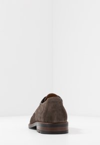 Chaussure en suède marron avec un bout arrondi, un dessus texturé et un petit talon en bois. Présente une doublure intérieure noire contrastante.