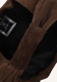 Bruine suède handtas met een zachte textuur, geplooid ontwerp en een zwarte binnenkant. Voorzien van een platte schouderband en een logo-label dat zichtbaar is aan de binnenkant.