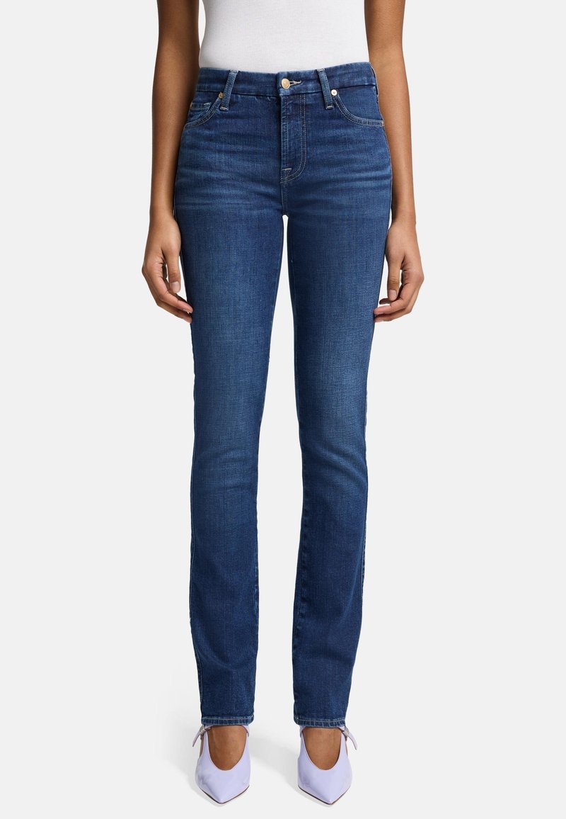 Jean en denim bleu foncé avec une silhouette ajustée, taille haute et détails de couture subtils. Associé à des chaussures pointues de couleur violet clair.
