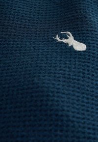 Dark blue textured fabric with a honeycomb pattern, featuring a white embroidered deer design in the lower corner.