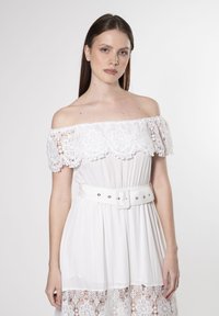 Weißes schulterfreies Kleid mit Spitze, elastischem Taillenbund und einem passenden breiten Gürtel. Verfügt über filigrane Spitzenmuster am Saum.