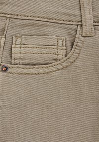 Beidzīgs džinsa audums tuvplānā, kurā redzams kabata, kontrastējoša šuvuma un maza metāla kniedes. Auduma tekstūra ir gluda ar smalku austu rakstu.