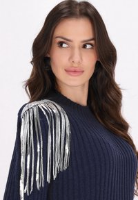 Pull en tricot navy à côtes avec un détail de franges argentées sur l'épaule gauche. Texture en tricot avec un col rond et des manches longues.