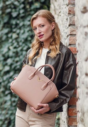 Beige leather handbag with two handles and a gold accent, featuring a structured shape and smooth texture. Set against a stone wall.
