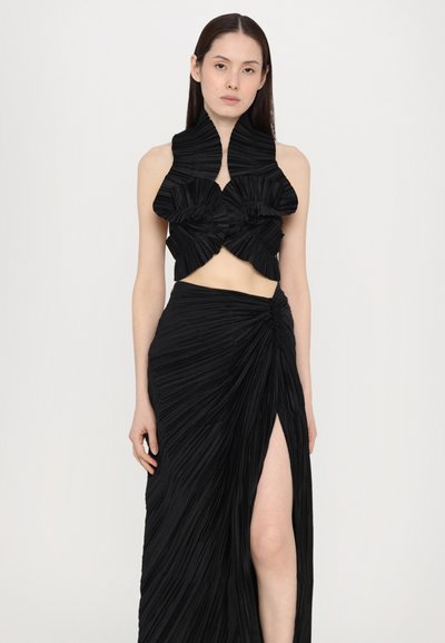 Black pleated dress featuring a cropped style top with asymmetrical ruffles and a high-slit skirt, showcasing smooth, draped textures.