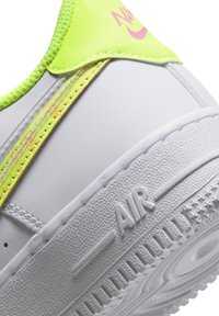 Gros plan de la semelle blanche d'une basket avec le texte "AIR" embossé et des détails néon jaune-vert et rose sur le col du talon.