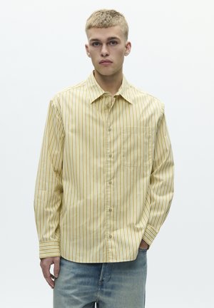 Gulstribet langærmet skjorte med knapper foran, lomme på venstre side og krave, kombineret med lyseblå denimjeans.