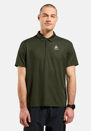 Mann trägt dunkelgrünes kurzärmeliges Polohemd mit Odlo-Logo, schwarze Hose und Smartwatch, stehend vor schlichtem hellem Hintergrund.