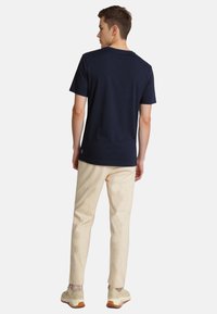 Marineblå bomulds T-shirt med rund hals, korte ærmer og lige kant, parret med lyse beige bukser og neutrale sneakers.