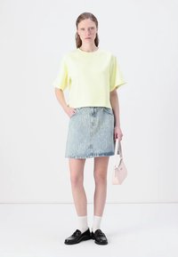 Κίτρινο κοντό μπλουζάκι, τζιν φούστα με ανοιχτό μπλε λογότυπο, λευκές κάλτσες, μαύρα παπούτσια και μια μικρή ροζ τσάντα.