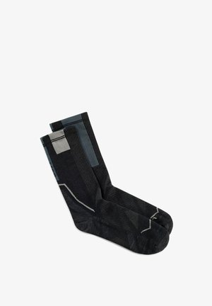 Paire de chaussettes noires avec motifs géométriques gris, posées à plat sur un fond blanc.