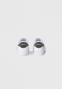 Valged tossud tekstureeritud valge tallaga ja halli kannaga. Kannal on "LACOSTE" logoga kaunistus ja küljel reljeefne logo.