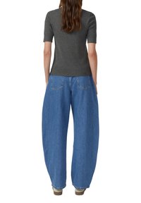 Grijze aansluitende top met korte mouwen gecombineerd met oversized blauwe spijkerbroeken. De jeans hebben een hoge taille en achterzakken.