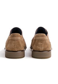 Chaussures en daim marron avec un bout rond, présentant un profil bas et une semelle en caoutchouc rayée. L'intérieur est doublé de tissu bleu marine, ajoutant un contraste.