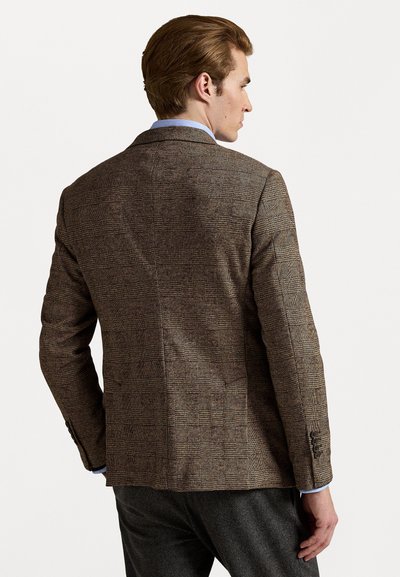 Blazer marrón en espiga con un corte ajustado, que presenta hombros estructurados, cierre de dos botones y costuras detalladas, combinado con pantalones grises.