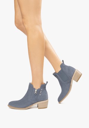 Blue suede ankle boots with a low stacked heel, zip closure, and elastic side panels; textured upper with perforated detailing and pull tab.