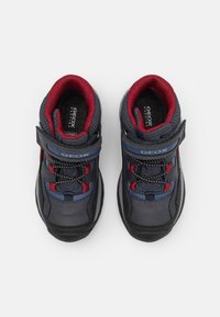 Ciemnoniebieskie buty typu high-top z czerwonymi akcentami, siateczkowym wykończeniem, elastycznymi sznurowadłami i rzepem. Teksturowana gumowa podeszwa dla lepszej przyczepności.