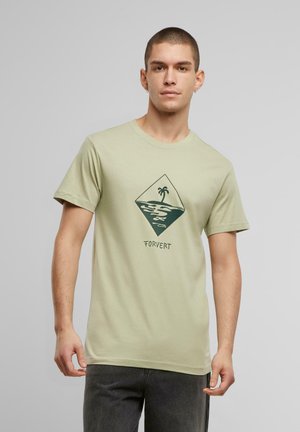 Lys grøn bomulds t-shirt med korte ærmer, der pryder et mørkegrønt diamantgrafik af et palmetræ over stiliserede bølger og teksten "FORVERT".