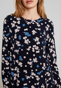 Blommig klänning i marinblått tyg med små vita och blå blommor. Långa ärmar, rund halsringning och en mjuk, slät textur.
