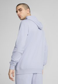 Lys blå hoodie lavet af blødt stof, med en hætte der kan justeres med snor, ribbede manschetter og en afslappet pasform. Bagsiden viser minimal detaljer.