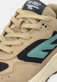 Μπεζ αθλητικό παπούτσι με επάνω μέρος από δίχτυ και ναυτικές λεπτομέρειες. Διαθέτει τυρκουάζ λογότυπο, στρογγυλά κορδόνια και υφή στη σόλα. Κατασκευασμένο από δέρμα σουέτ και αναπνεύσιμα υλικά.