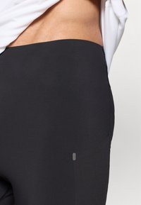 Μαύρο αθλητικό κολάν με ομαλή, ελαστική υφή και πλαϊνή τσέπη. Οι ραφές είναι εμφανείς στη μέση και στο πόδι.