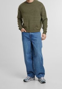 Olive green knitted sweater, relaxed fit. Light blue wide-leg jeans. Grey sneakers with blue accents. Simple, casual outfit with textured materials.