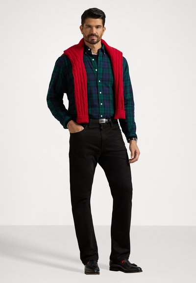 Green plaid button-up shirt, red cable-knit sweater draped over shoulders, black jeans, black shoes. Simple, classic casual outfit.