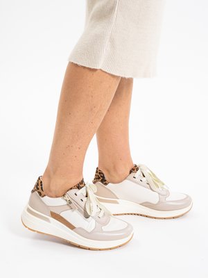 Osoba nosící béžové a bílé tenisky s leopardím vzorem a silnými bílými podrážkami, spojené s krémově zbarvenou sukní.