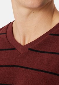 Maglione bordeaux a scollo a V con un tessuto testurizzato, caratterizzato da strisce orizzontali nere e un colletto a maglia. Dettaglio ravvicinato del scollo.