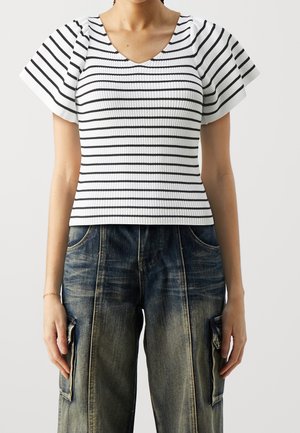 Weißes geripptes Oberteil mit schwarzen horizontalen Streifen, kurzen ausgestellten Ärmeln und V-Ausschnitt. Kombiniert mit hoch taillierten blauen Denim-Cargo-Hosen.
